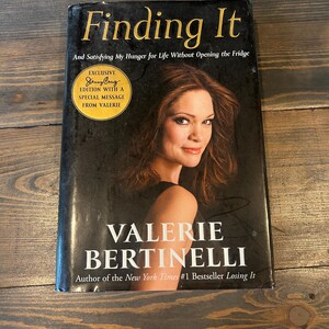May include: A hardcover book titled "Finding It" by Valerie Bertinelli. The cover features a photo of Bertinelli and the text "And Satisfying My Hunger for Life Without Opening the Fridge." An exclusive edition sticker is also visible.