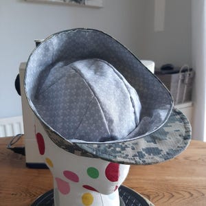 May include: A grey and green patterned hat with a grey fabric lining. The hat is on a mannequin head.
