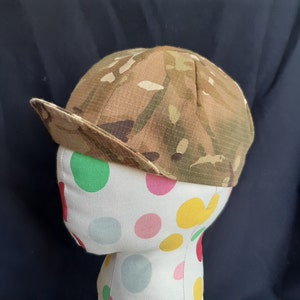 May include: A camouflage patterned baseball cap with a curved brim. The cap is on a white mannequin head with colourful polka dots.