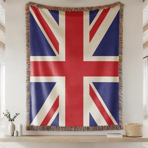 Pode incluir: Um grande cobertor tecido com o design da bandeira Union Jack. A bandeira exibe as cores vermelha, branca e azul. O cobertor tem uma borda com franjas e está pendurado em uma parede.