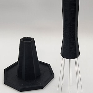 May include: A black plastic tool with a hexagonal base and a long, tapered handle. The handle has a series of thin, metal needles extending from the bottom.