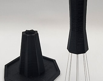 May include: A black plastic tool with a hexagonal base and a long, tapered handle. The handle has a series of thin, metal needles extending from the bottom.