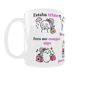 Pode incluir: Uma caneca de cerâmica branca com ilustrações de desenhos animados e texto em espanhol. Os gráficos mostram uma personagem com um laço cor-de-rosa, primeiro triste sob uma nuvem de chuva com o texto 'Estaba triste?', depois feliz com sacos de compras e o texto 'Pero me compré algo'.
