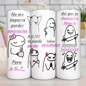 Pode incluir: Um copo cilíndrico branco com desenhos de personagens em linhas pretas e texto em rosa em espanhol. O design inclui várias figuras expressivas, algumas segurando facas, com frases como No me importa perder amistades e Así que es Amistad o Muerte.