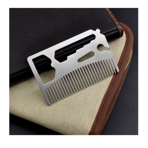 May include: A silver multi-tool card with a comb, bottle opener, and other tools. The card is lying on a brown and beige fabric surface.