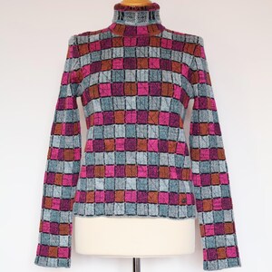 May include: A long-sleeved turtleneck sweater with a checkered pattern in shades of pink, blue, and brown.