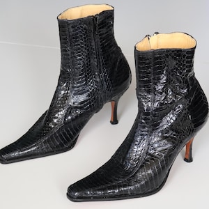 Puede incluir: Un par de botines negros con textura de reptil. Los botines tienen punta afilada, tacones de aguja y cremalleras laterales. Los tacones miden aproximadamente 7,6 cm de alto. El forro interior es de color beige claro.