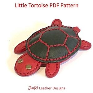 May include: A red leather tortoise with a black leather shell and red stitching. The tortoise has two gold-coloured buttons for eyes.