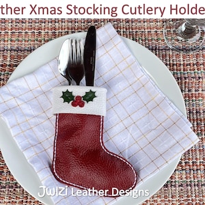 May include: A red leather Christmas stocking cutlery holder with white stitching, holding a fork, spoon, and knife. The stocking has a white cuff with holly and berry accents. The text "Leather Xmas Stocking Cutlery Holder" is at the top.