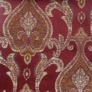 Puede incluir: Primer plano de una tela burdeos con un estampado de damasco dorado y crema. El diseño presenta motivos florales y de cachemira ornamentados y arremolinados. La tela tiene un ligero brillo, lo que sugiere una textura lujosa, y es adecuada para tapicería o proyectos decorativos.