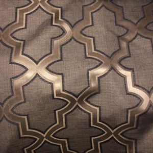May include: Close-up of a fabric with a repeating geometric pattern. The design features a dark grey background with a gold and dark grey quatrefoil pattern. The fabric has a textured appearance.