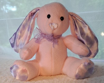 Conejito de peluche con peso, de color rosa y morado, con orejas arrugadas.