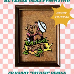 May include: Reverse glass painting in a brown frame featuring an Ed Hardy "Father" design. The artwork depicts a sailor with a banner that reads "FATHER". The painting is ready to hang.