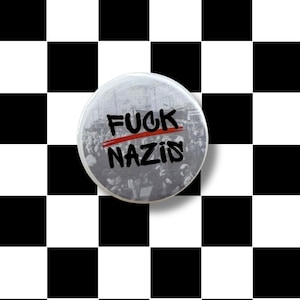 May include: A round button with the text "FUCK NAZIS" in black, with the word "NAZIS" crossed out in red. The button features a grayscale image of a crowd. The background is a black and white checkerboard pattern.