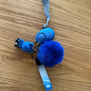 May include: A blue keychain with a small blue animal charm, a blue pom-pom, and a blue personal alarm with a silver ring.