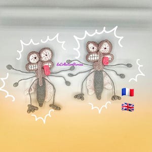 Peut inclure: Deux jouets moustiques en crochet gris avec des langues roses qui dépassent. Les jouets ont de grands yeux et sont entourés d'une ligne blanche en zigzag.