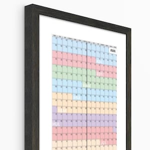 以下が含まれることがあります： 暗い木目のフレームに入った壁掛けカレンダー。カレンダーは、月と日を表すカラフルなブロックのグリッドが特徴です。色はピンク、青、緑、黄色、紫などです。カレンダーは白い壁に掛けられています。