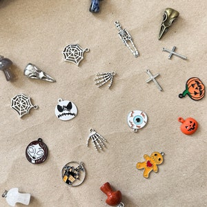 May include: A collection of silver and gold Halloween-themed charms, including a witch's hat, a skeleton, a spider web, a skull, a pumpkin, a gingerbread man, and a hand.