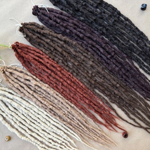May include: A set of six long, synthetic dreadlocks in various shades of brown, red, and beige. The dreadlocks are arranged in a fan shape, with the darkest color at the top and the lightest color at the bottom.