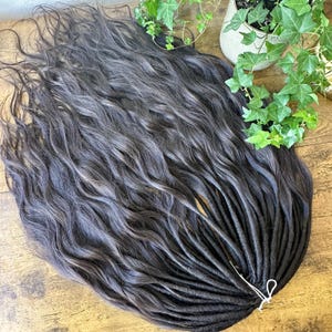 Könnte beinhalten: Ein Satz langer, dunkelbrauner Dreadlocks mit grauen Highlights. Die Dreadlocks sind mit einem weißen Band zusammengebunden.