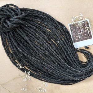 Könnte beinhalten: Schwarze synthetische Dreadlocks mit einer strukturierten Oberfläche. Die Dreadlocks sind lang und dick und in einem lockeren, fließenden Stil angeordnet.