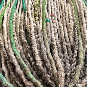 May include: A bundle of synthetic dreadlocks in shades of gray, white, and green. The dreadlocks are tied together with a black ribbon.