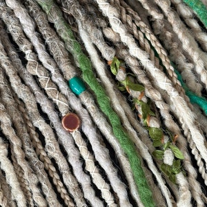 May include: Close-up of a collection of synthetic dreadlocks in shades of beige and green. The dreadlocks are decorated with small beads and fabric flowers.