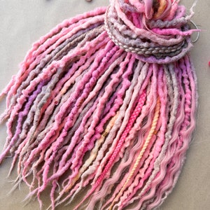 May include: A set of pink, peach, and beige synthetic dreadlocks with a braided headband. The dreadlocks are made of kanekalon hair and are approximately 24 inches long.