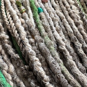 May include: A close-up of a bundle of synthetic dreadlocks in shades of white and green. The dreadlocks are made of a soft, textured material and are arranged in a neat, organized pattern.