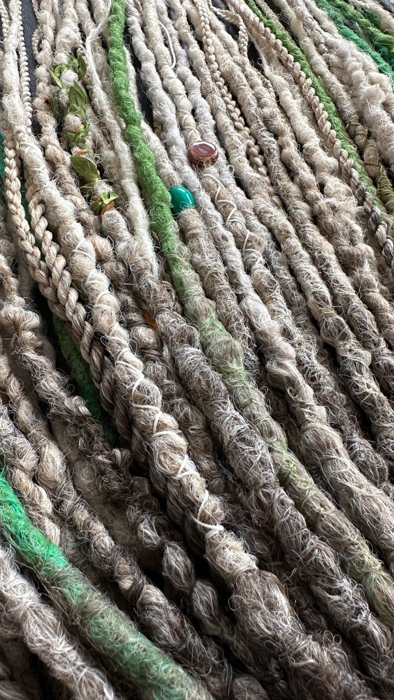May include: A close-up of a bundle of synthetic dreadlocks in shades of white and green. The dreadlocks are made of a soft, textured material and are arranged in a neat, organized pattern.
