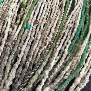 May include: A collection of synthetic dreadlocks in shades of gray, white, and green. The dreadlocks are arranged in a fan shape and have beads and other decorative elements.