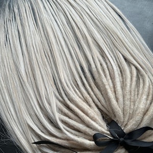 May include: A set of long, white and light blonde synthetic dreadlocks tied together with a black ribbon.