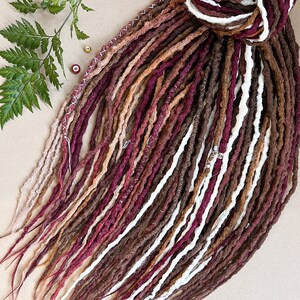 May include: A set of brown, white, and burgundy synthetic dreadlocks. The dreadlocks are made of a soft, textured material and are tied together at the top.
