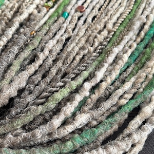 May include: A bundle of synthetic dreadlocks in shades of gray, green, and white. The dreadlocks are made of a soft, fuzzy material and are ready to be installed.