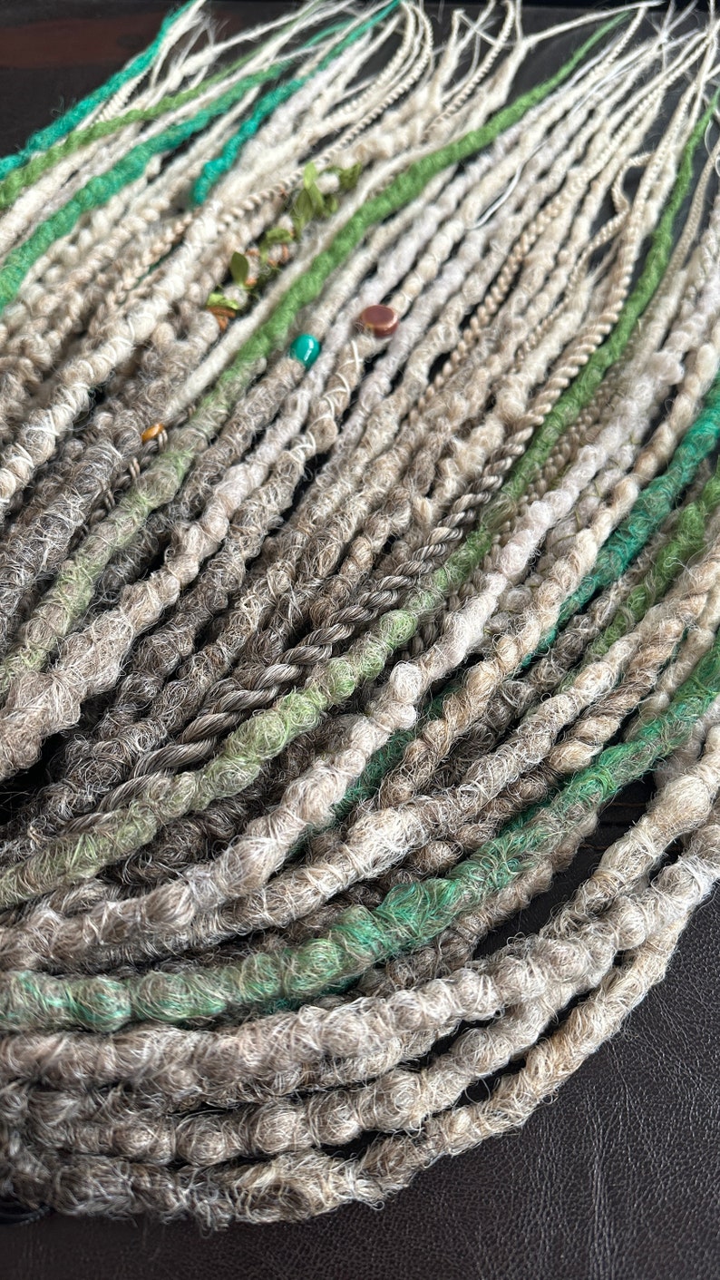 May include: A bundle of synthetic dreadlocks in shades of gray, green, and white. The dreadlocks are made of a soft, fuzzy material and are ready to be installed.