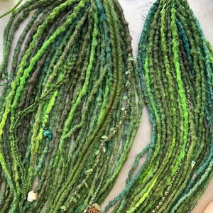 Puede incluir: Un conjunto de rastas verdes y marrones con diferentes tonos de verde. Algunas rastas están adornadas con pequeños elementos decorativos, incluyendo cuentas y detalles en forma de hojas. Las rastas están dispuestas sobre una superficie neutra.