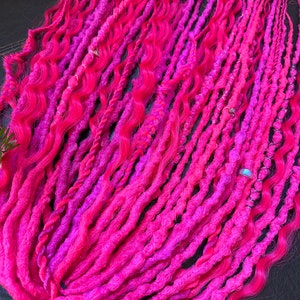 May include: A set of pink and magenta synthetic dreadlocks with beads. The dreadlocks are wavy and have a ombre effect.