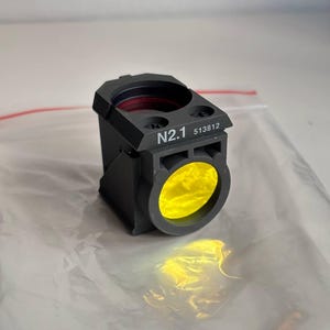 May include: A black rectangular device with a yellow lens and the text "N2.1 513812". The device has a red interior and is set against a white background.
