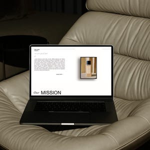 以下が含まれることがあります： 「we are good feet」と「Our MISSION」のテキストが表示されたウェブサイトを映す黒いノートパソコンが、ライトグレーの革張りのアームチェアに置かれています。ウェブサイトには製品画像と説明文が含まれています。