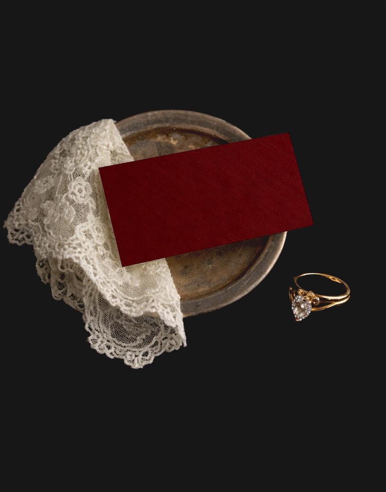 May include: A gold ring with a heart-shaped diamond is placed near a red card and a vintage silver plate with a white lace doily. The ring has a delicate design, and the card has a textured surface. The items are arranged on a dark background.