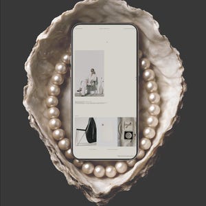 May include: A smartphone displaying a website, nestled in a large oyster shell, surrounded by a strand of pearls. The shell is off-white with a textured surface. The pearls are a creamy white color. The background is a dark gray.