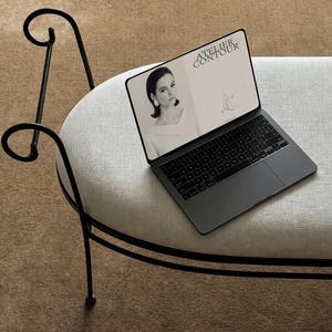 Puede incluir: Un ordenador portátil gris oscuro está sobre un banco tapizado gris claro con patas de metal negro. La pantalla del portátil muestra una imagen en blanco y negro con el texto "ATELIER CONTOUR" y un retrato de mujer.