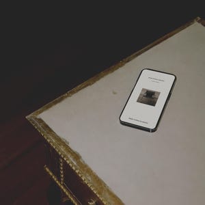 May include: A black smartphone displaying a white screen with the text "atolie mockup collection" and "Atelier Contour by elmore" along with a small black and white square image of a chair, positioned on a light-colored surface with gold trim.