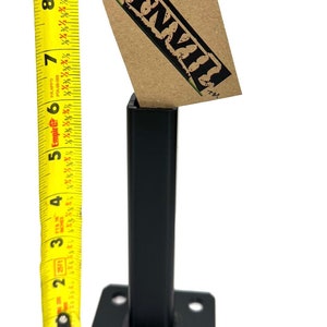 May include: A black metal post with a square base and four holes. The post is about 9 inches tall. A brown paper tag with the word "ANVIL" is attached to the post.
