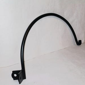May include: Black metal hook with a curved arm and a flat base. The hook is designed to hang items on a wall.