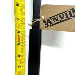 May include: A black metal rod with a black plastic sleeve, measured with a yellow tape measure that reads 6 inches. The rod is labeled "ANVIL".