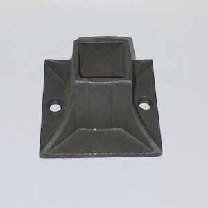May include: A black metal square base with a square hole in the center. The base has four holes on the sides for mounting.
