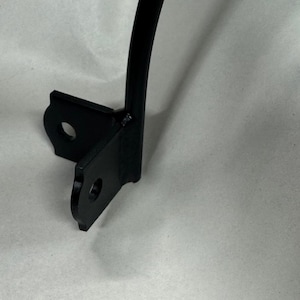 May include: A black metal bracket with two mounting holes and a curved arm. The bracket is designed to attach to a surface and support an object. The metal has a matte finish.