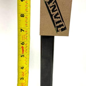 May include: A black metal post with a square base and a tag that reads "ANVIL". The post is approximately 10 inches tall, as measured by a yellow tape measure.