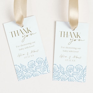 May include: Two light blue gift tags with gold text and a seashell design. The tags read "THANK you" and include the text "For showering our baby with love!" and names and a date. Each tag is attached to a gold ribbon.